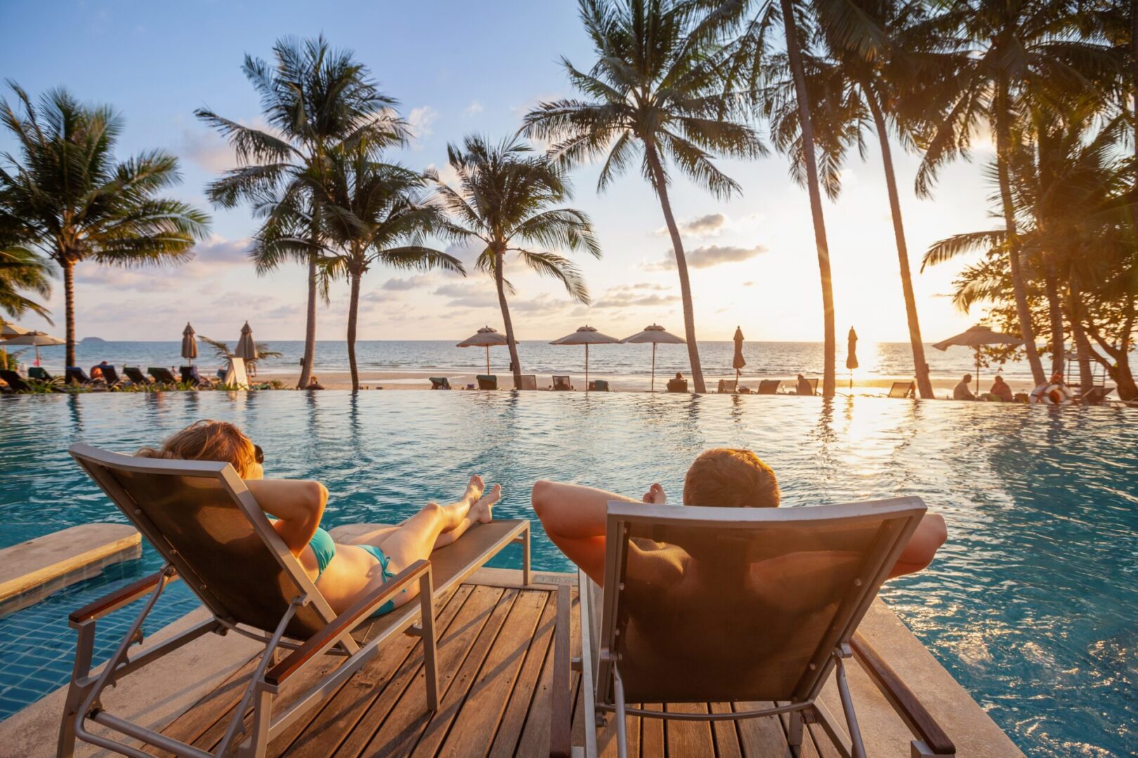 Two people sitting on lawn chairs near a pool.