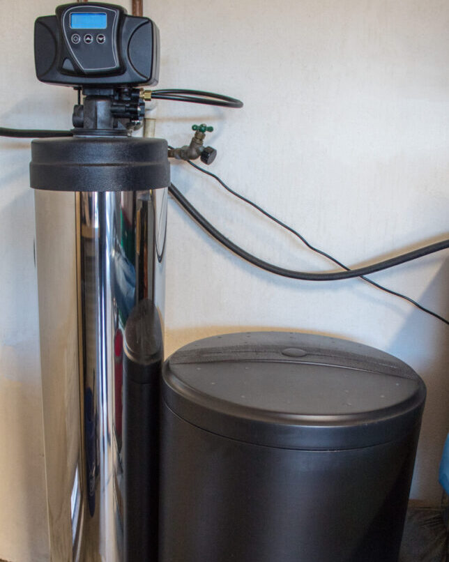 A black trash can sitting next to a shiny metal water filter.