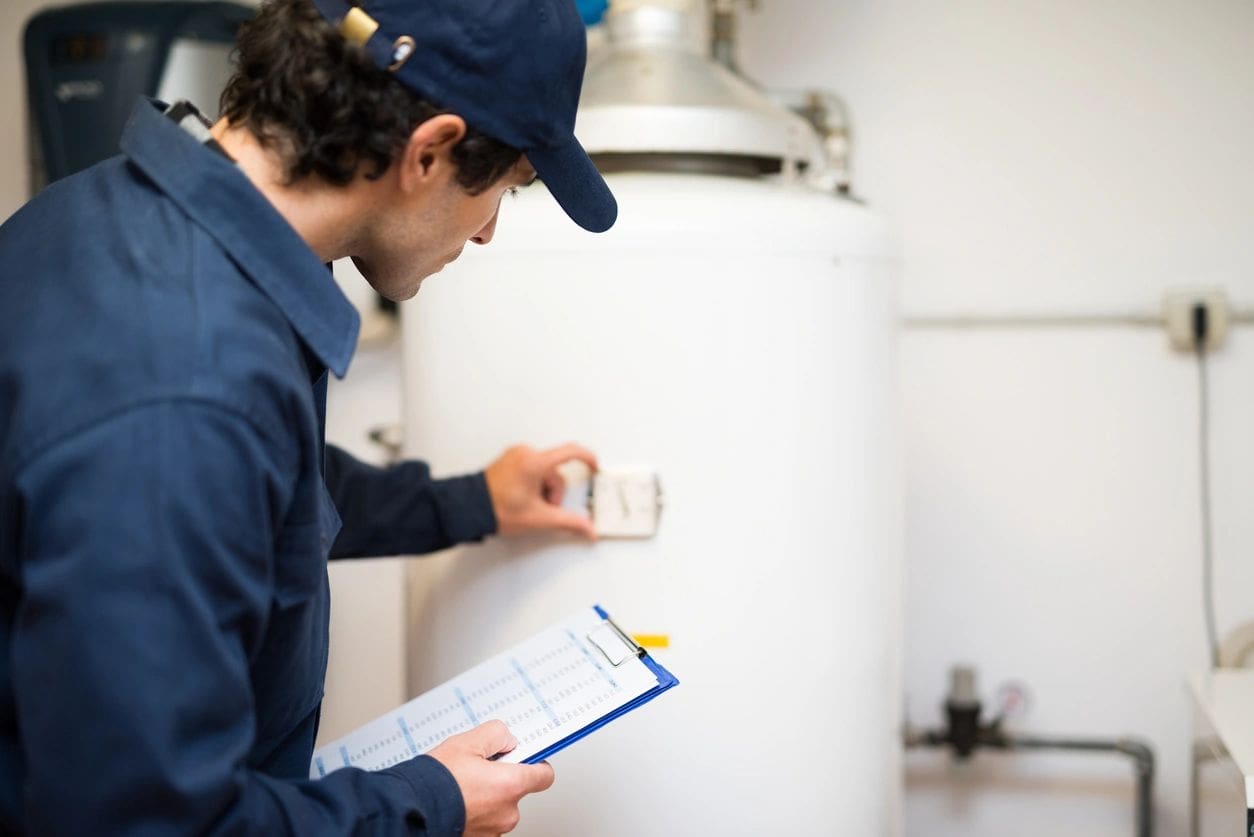 A man in blue shirt holding clipboard near water heater.